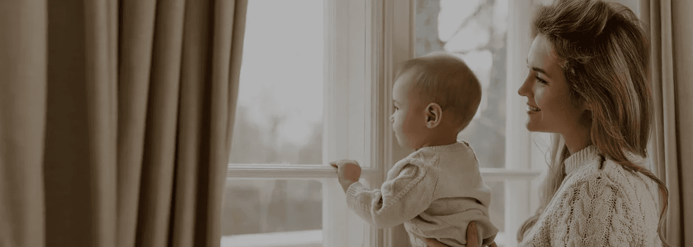 A person holding a baby looks out a window.